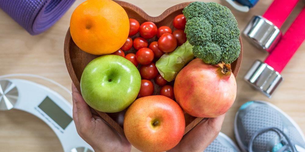 水果和蔬菜放在一个心形的碗里，周围是锻炼设备